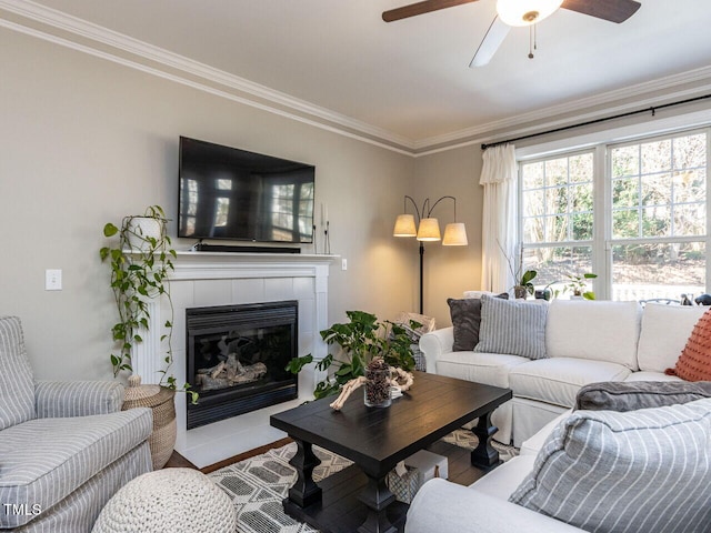 living area featuring a tiled fireplace, crown molding, and a ceiling fan