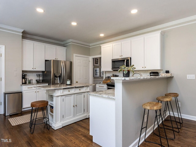 kitchen featuring a peninsula, appliances with stainless steel finishes, a breakfast bar, and white cabinets