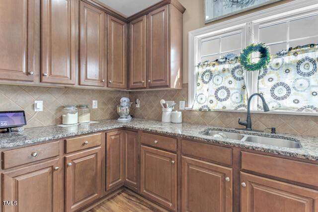 kitchen with brown cabinets, a sink, backsplash, and light stone countertops