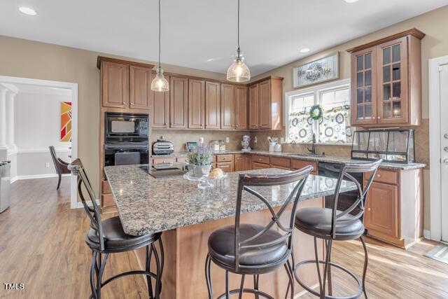 kitchen with light stone counters, a breakfast bar area, decorative backsplash, light wood-style floors, and black appliances