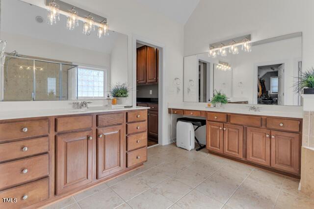 full bathroom featuring a stall shower, lofted ceiling, two vanities, and a sink