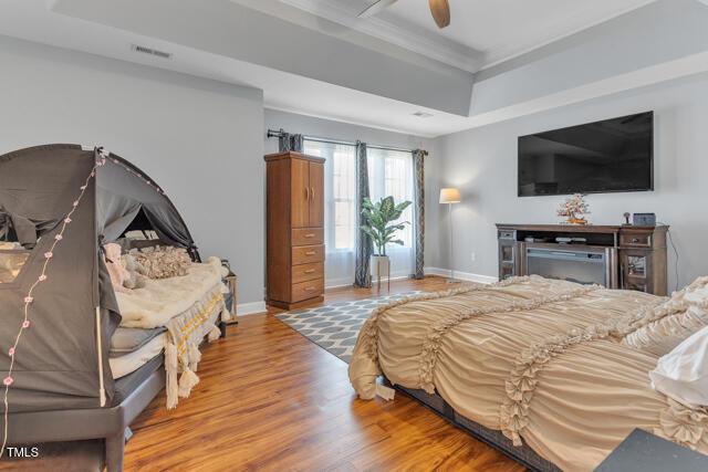 bedroom featuring crown molding, a raised ceiling, visible vents, wood finished floors, and baseboards