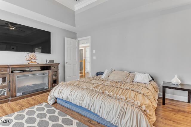 bedroom featuring ornamental molding, a glass covered fireplace, baseboards, and wood finished floors