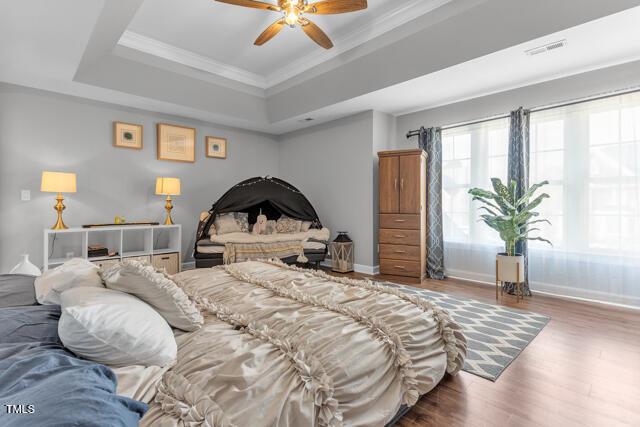 bedroom featuring a raised ceiling, visible vents, ornamental molding, wood finished floors, and baseboards