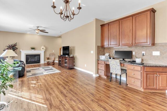 living room with light wood-style floors, a glass covered fireplace, built in study area, baseboards, and ceiling fan with notable chandelier