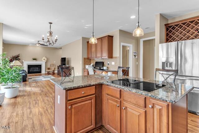 kitchen featuring black electric stovetop, a fireplace, a kitchen island, stainless steel fridge with ice dispenser, and light stone countertops