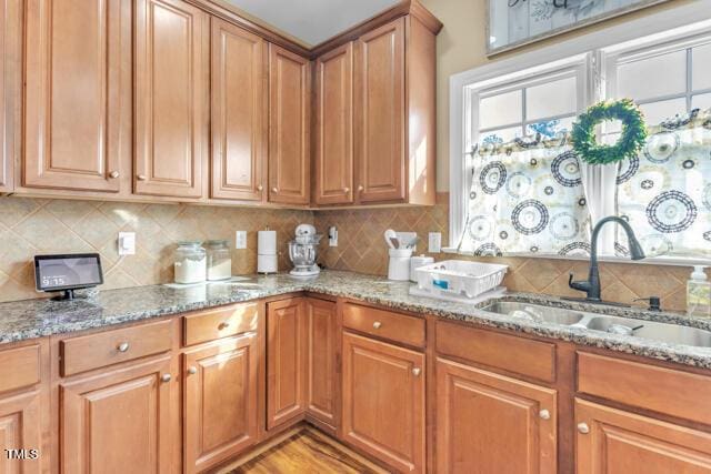 kitchen featuring light wood finished floors, brown cabinetry, light stone counters, a sink, and backsplash