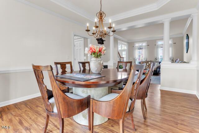 dining room with a raised ceiling, crown molding, light wood-style flooring, and ornate columns