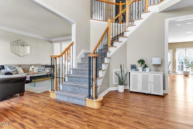 stairway with a high ceiling, wood finished floors, visible vents, baseboards, and crown molding