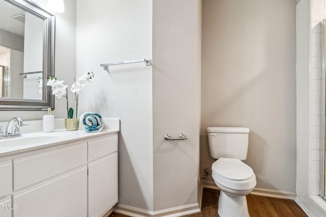 bathroom featuring baseboards, toilet, wood finished floors, walk in shower, and vanity