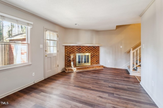 unfurnished living room featuring a brick fireplace, stairway, baseboards, and wood finished floors