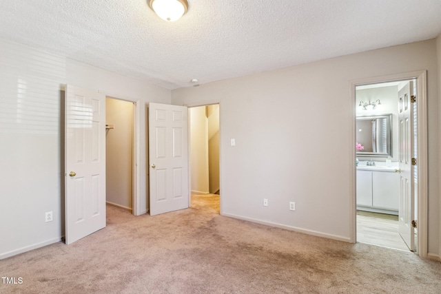 unfurnished bedroom with a textured ceiling, baseboards, ensuite bath, and light colored carpet