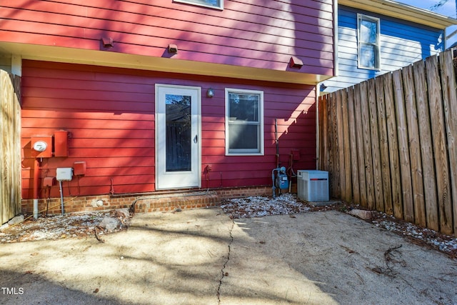 view of exterior entry with fence, central AC unit, and a patio