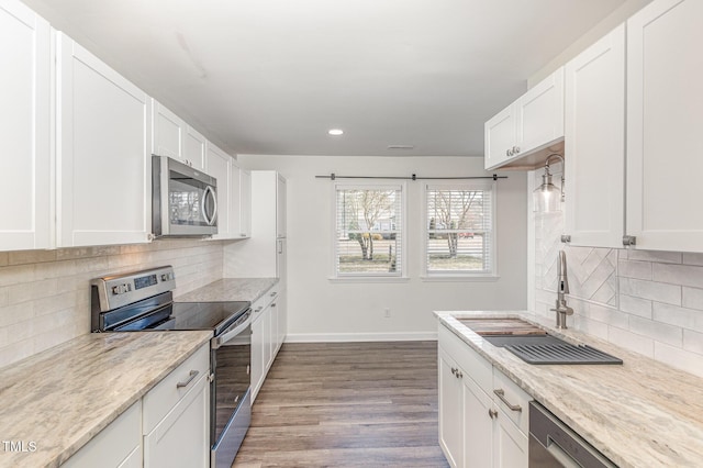 kitchen featuring wood finished floors, baseboards, a sink, white cabinets, and appliances with stainless steel finishes