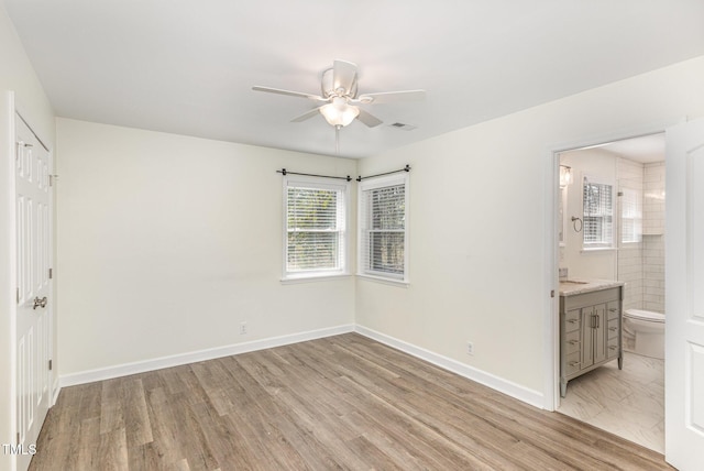 unfurnished bedroom with visible vents, connected bathroom, light wood-style floors, and baseboards