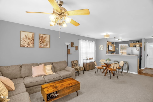 living room featuring ceiling fan, baseboards, and light colored carpet