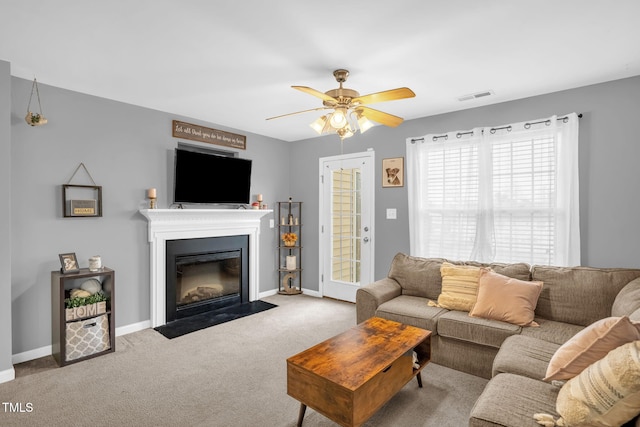 living room featuring visible vents, baseboards, a ceiling fan, a fireplace with flush hearth, and carpet