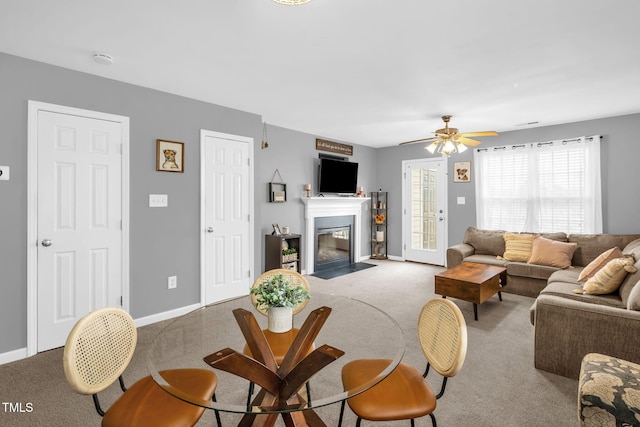 living area with carpet floors, a fireplace with flush hearth, a ceiling fan, and baseboards