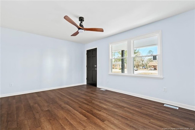 spare room with dark wood-style floors, ceiling fan, visible vents, and baseboards