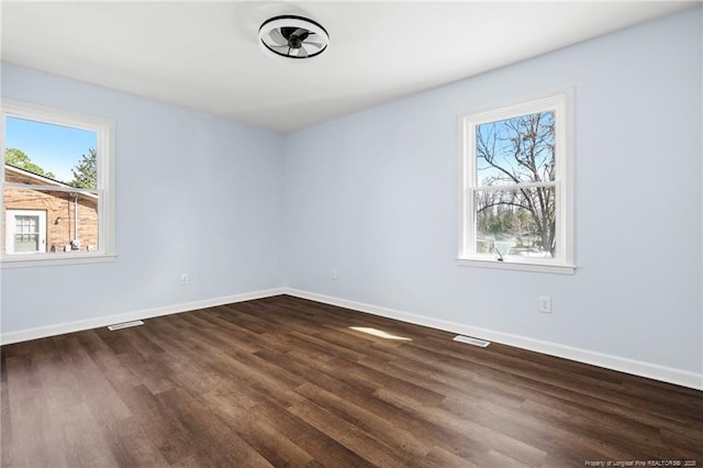 spare room featuring dark wood-type flooring, visible vents, and baseboards