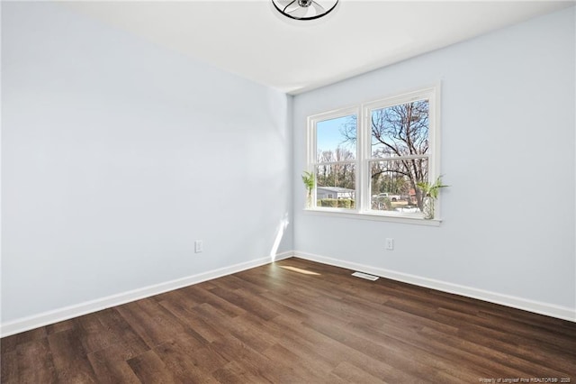 unfurnished room with dark wood-type flooring, visible vents, and baseboards