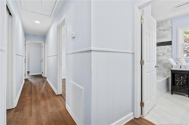 corridor with a wainscoted wall, wood finished floors, visible vents, and attic access