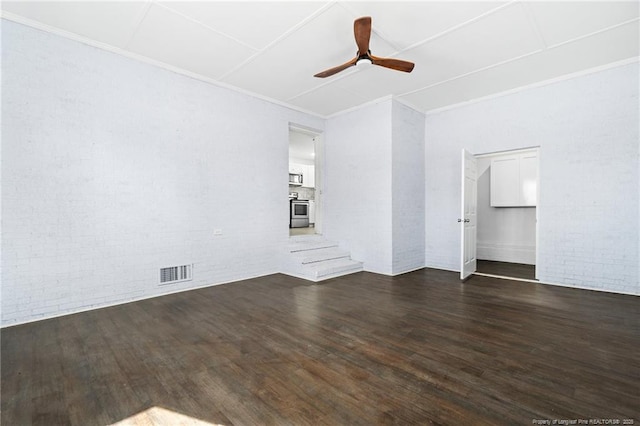 unfurnished room featuring brick wall, visible vents, dark wood finished floors, and a ceiling fan