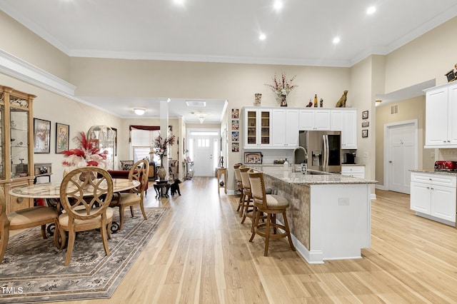 kitchen with an island with sink, ornamental molding, light wood-style flooring, white cabinets, and stainless steel fridge