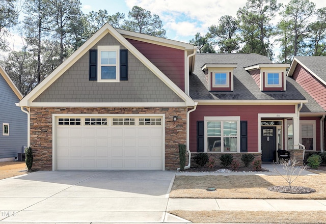 craftsman-style house featuring driveway, stone siding, cooling unit, a shingled roof, and a garage