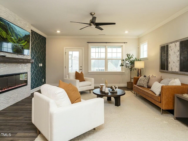 living area featuring wood finished floors, baseboards, ceiling fan, ornamental molding, and a large fireplace