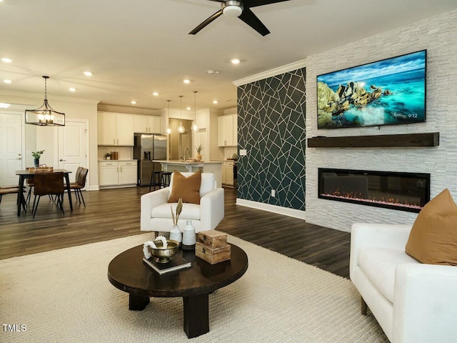 living area with crown molding, recessed lighting, ceiling fan with notable chandelier, and dark wood-type flooring