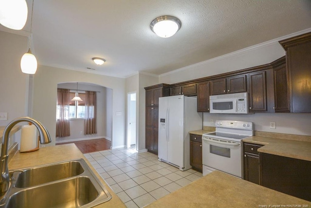 kitchen with dark brown cabinetry, white appliances, light tile patterned floors, and a sink