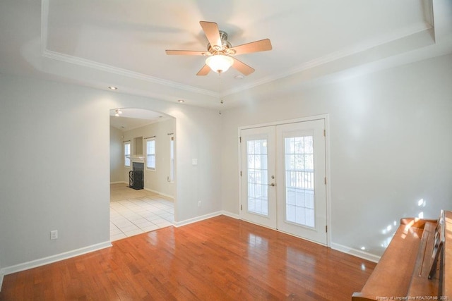 unfurnished room featuring baseboards, arched walkways, wood finished floors, a tray ceiling, and french doors