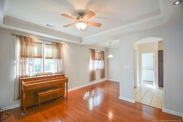 empty room with arched walkways, wood finished floors, visible vents, ornamental molding, and a tray ceiling