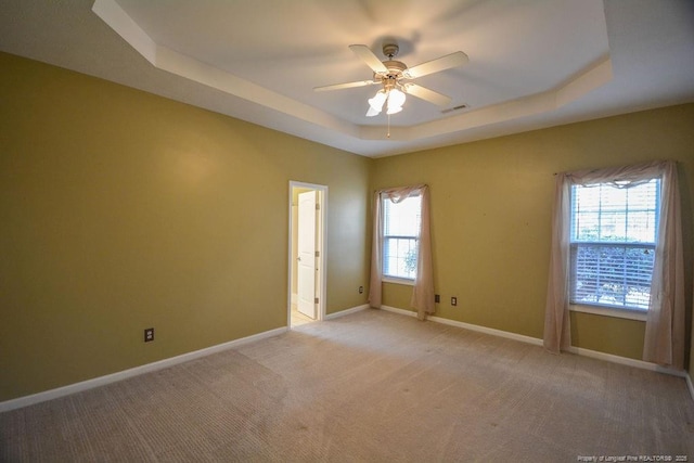 spare room featuring light carpet, visible vents, baseboards, a raised ceiling, and a ceiling fan