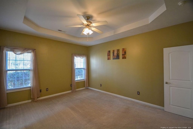 empty room with a ceiling fan, a tray ceiling, light colored carpet, and baseboards