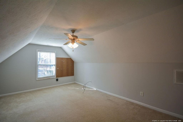 additional living space featuring a textured ceiling, lofted ceiling, light carpet, visible vents, and baseboards