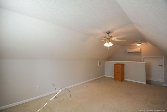 additional living space featuring a wall unit AC, baseboards, vaulted ceiling, and a textured ceiling