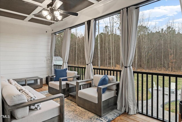 sunroom featuring ceiling fan, beamed ceiling, coffered ceiling, and a wooded view