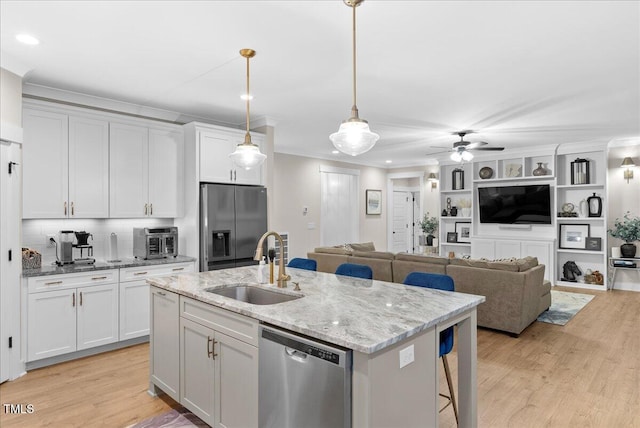 kitchen featuring light wood finished floors, appliances with stainless steel finishes, ornamental molding, a kitchen island with sink, and a sink