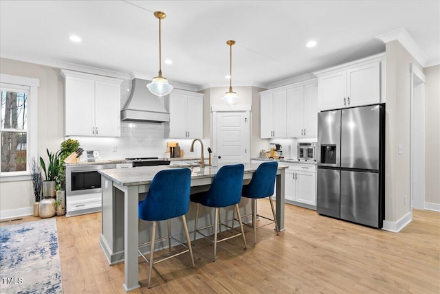 kitchen featuring premium range hood, white cabinetry, backsplash, stainless steel fridge with ice dispenser, and an island with sink