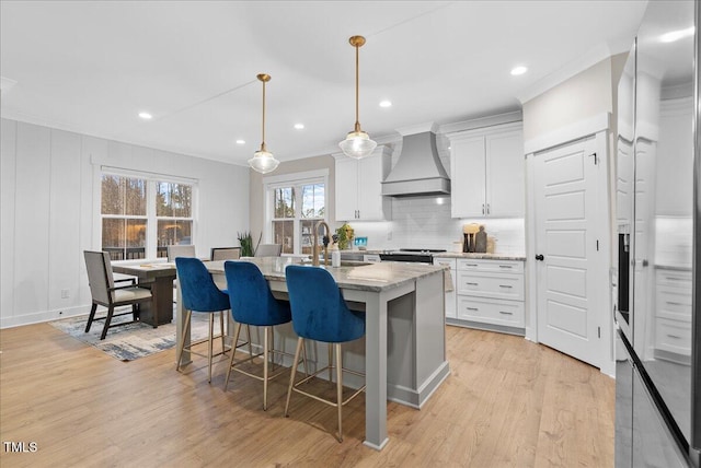 kitchen with light wood finished floors, tasteful backsplash, custom range hood, crown molding, and white cabinetry