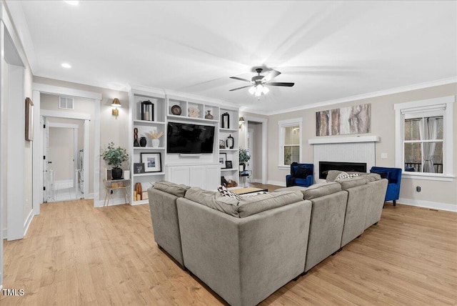 living area with ornamental molding, light wood-type flooring, visible vents, and a fireplace