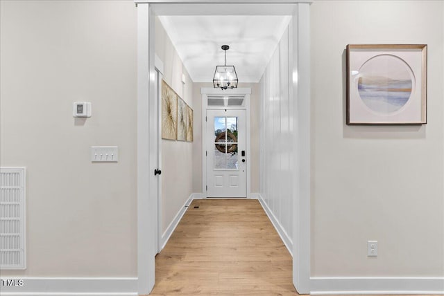 doorway featuring crown molding, a notable chandelier, light wood-style flooring, and baseboards