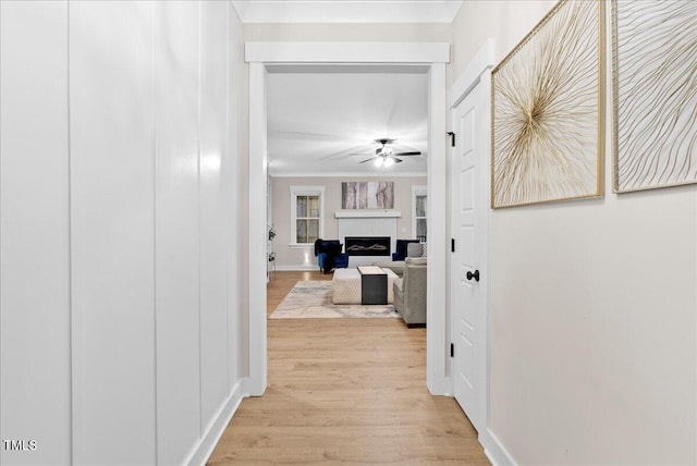 hall featuring crown molding, light wood-style flooring, and baseboards