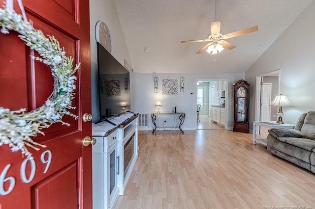 interior space with ceiling fan, a textured ceiling, light wood-style flooring, baseboards, and open floor plan