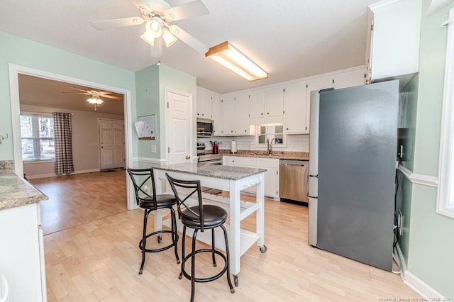 kitchen featuring light wood finished floors, decorative backsplash, appliances with stainless steel finishes, white cabinetry, and a sink