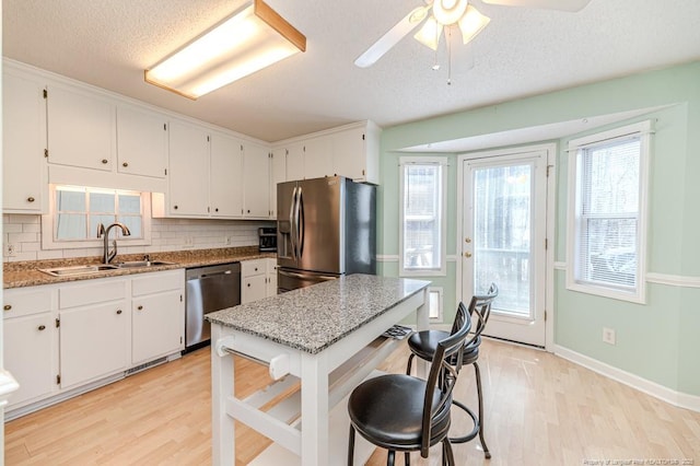 kitchen featuring light wood finished floors, appliances with stainless steel finishes, a sink, and white cabinetry