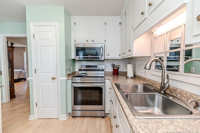 kitchen with stainless steel appliances, a sink, decorative backsplash, and light wood finished floors