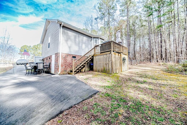 view of property exterior with brick siding, fence, stairway, and a wooden deck